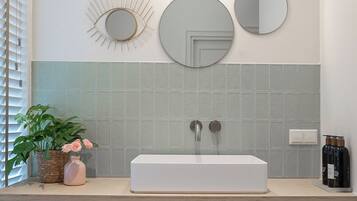 A bathroom with a white sink, two mirrors, a wall-mounted light, and a potted plant.