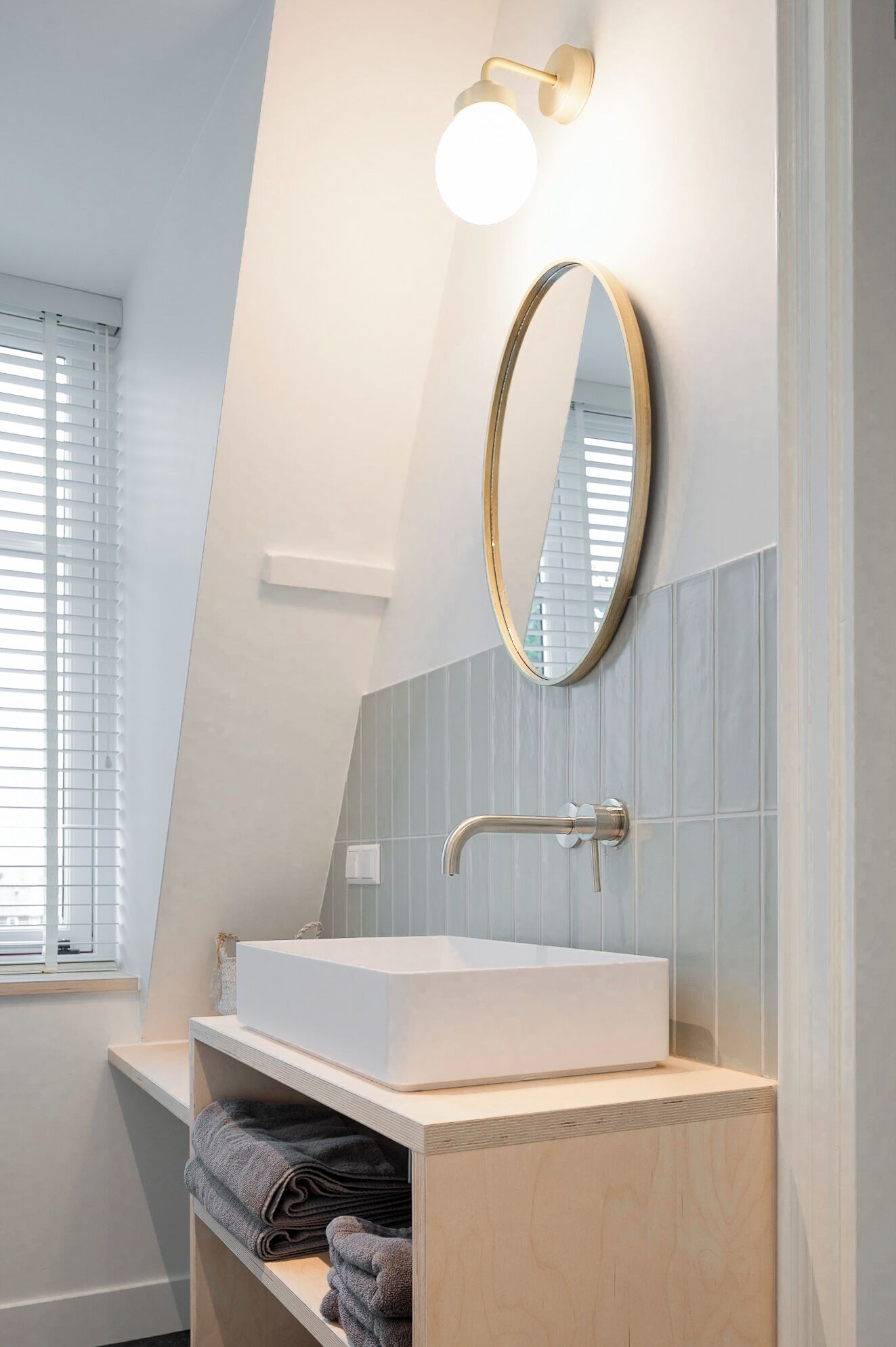 A modern bathroom with a white sink, a round mirror, and a light fixture above it.