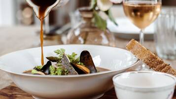 A dining table with a bowl of food, a glass of wine, and a hand pouring sauce.