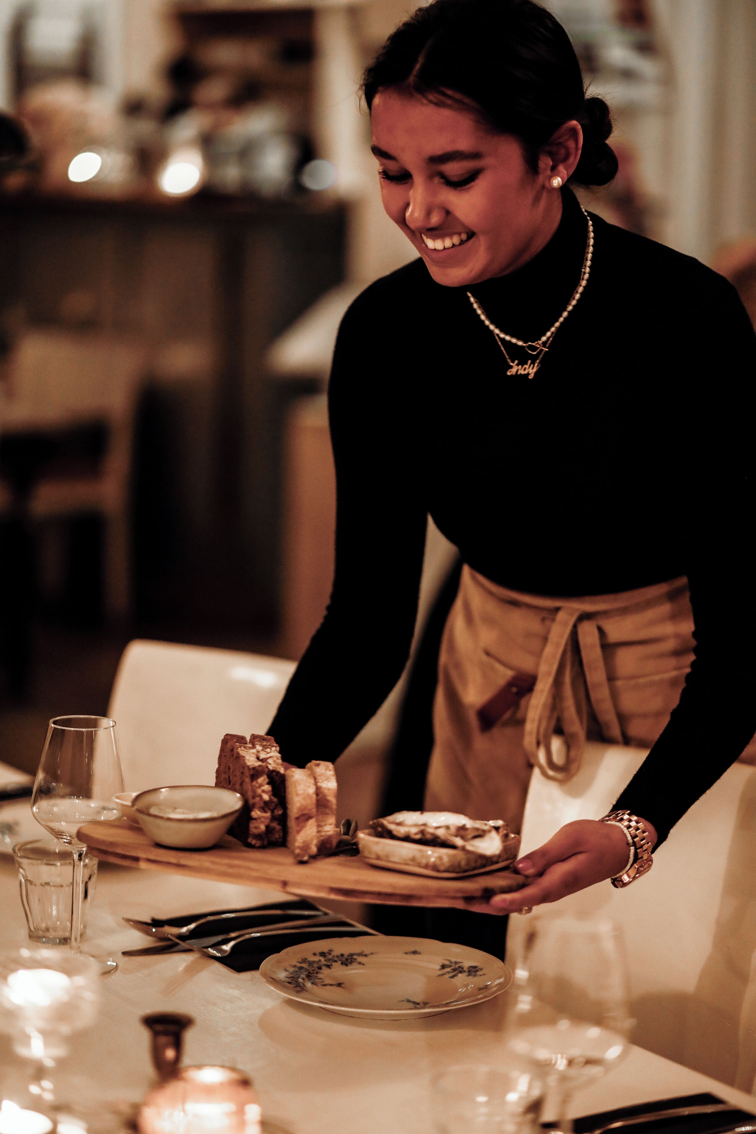 A person serving food at a table with plates, a glass, and cutlery.