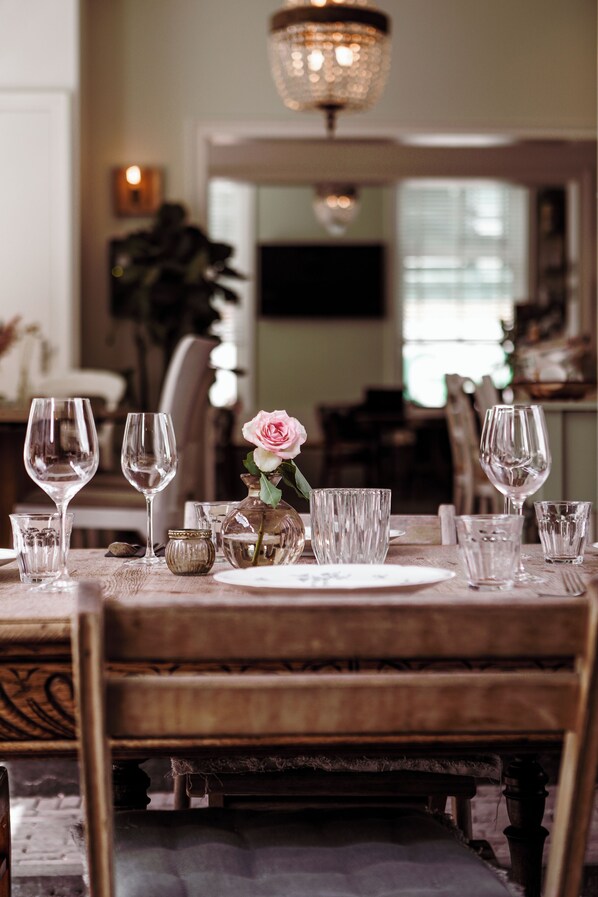 Una mesa de comedor dispuesta con copas de vino, un florero con una flor y una vela.