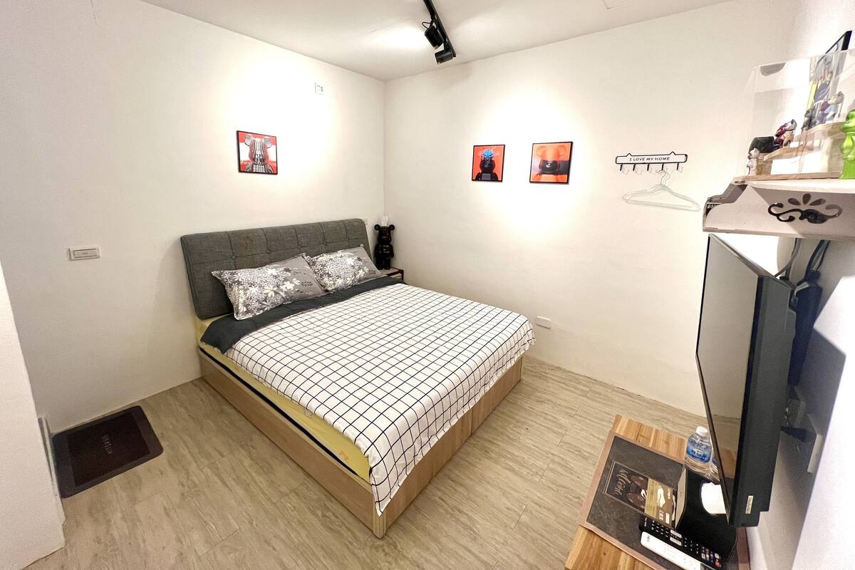 A bedroom with a bed, a bedside table, a TV, and wall art.