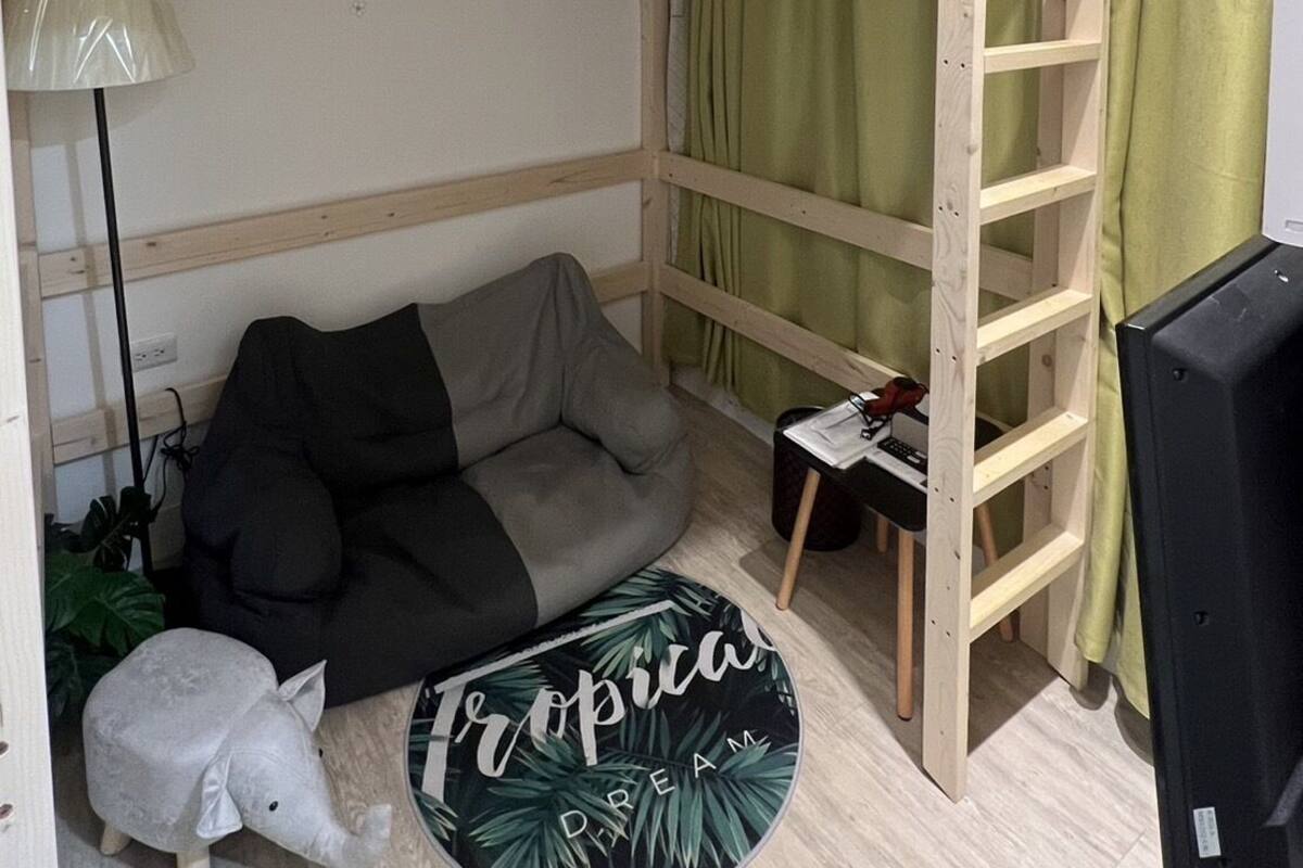 A bunk bed room with a ladder, a sofa, a lamp, and a small elephant figurine.
