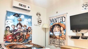 A bedroom with a bed featuring a One Piece themed bedspread, a wall-mounted air conditioner, a poster of a One Piece character, a 'Wanted' poster, and a television on a stand. - mimi cat house (Tainan)