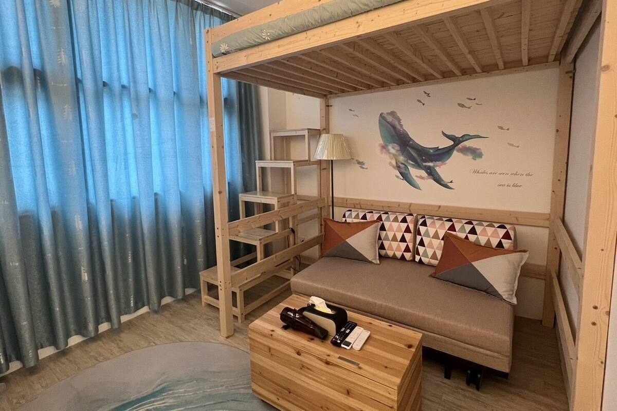 A room with a bunk bed, a sofa, a small table, and a wall with a whale mural.