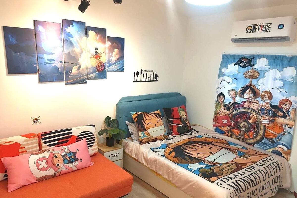 A bedroom with a bed featuring One Piece-themed bedding, a blue headboard, and a wall with One Piece artwork.