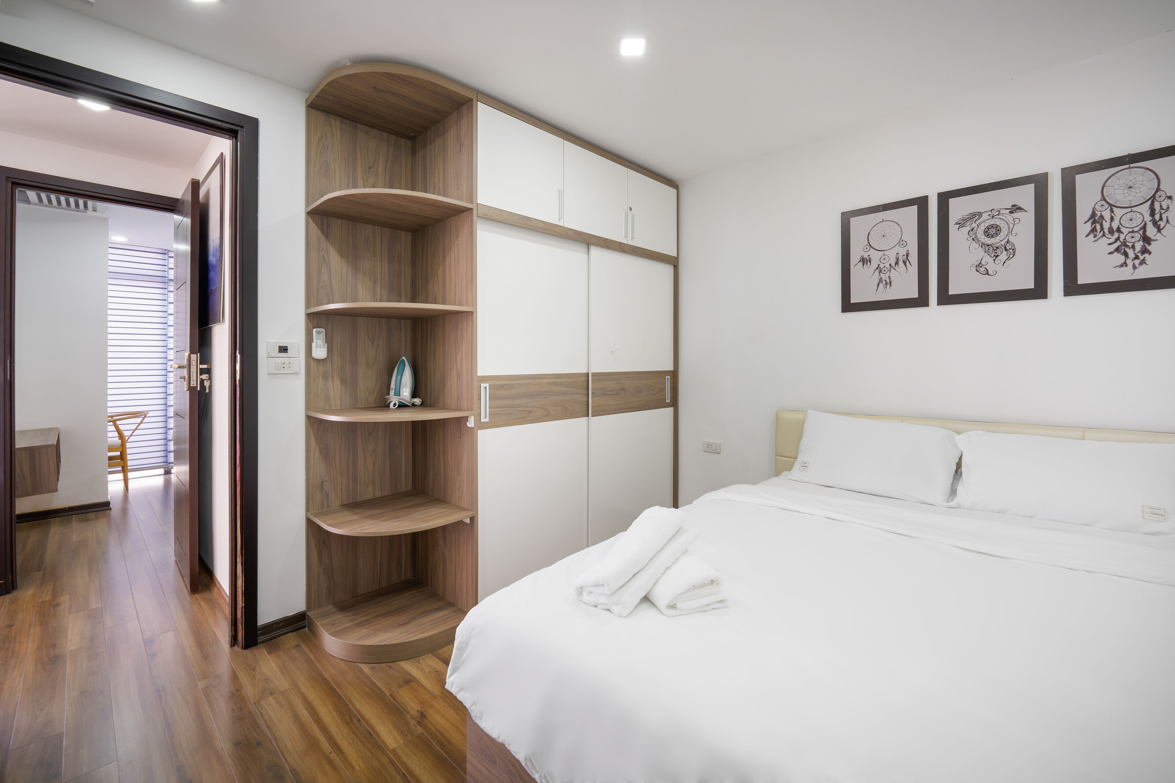 A modern bedroom with a wooden wardrobe, a bed with white linens, and three wall-mounted artwork.