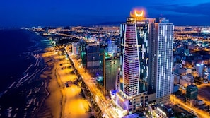 Ein Hochhaus-Hotel mit markanter Dachkonstruktion, neben einem Strand und einer Stadtansicht.