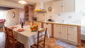 Una cucina accogliente con zona pranzo, caratterizzata da un forno a mattoni, mobili bianchi e una parete rivestita di piastrelle.