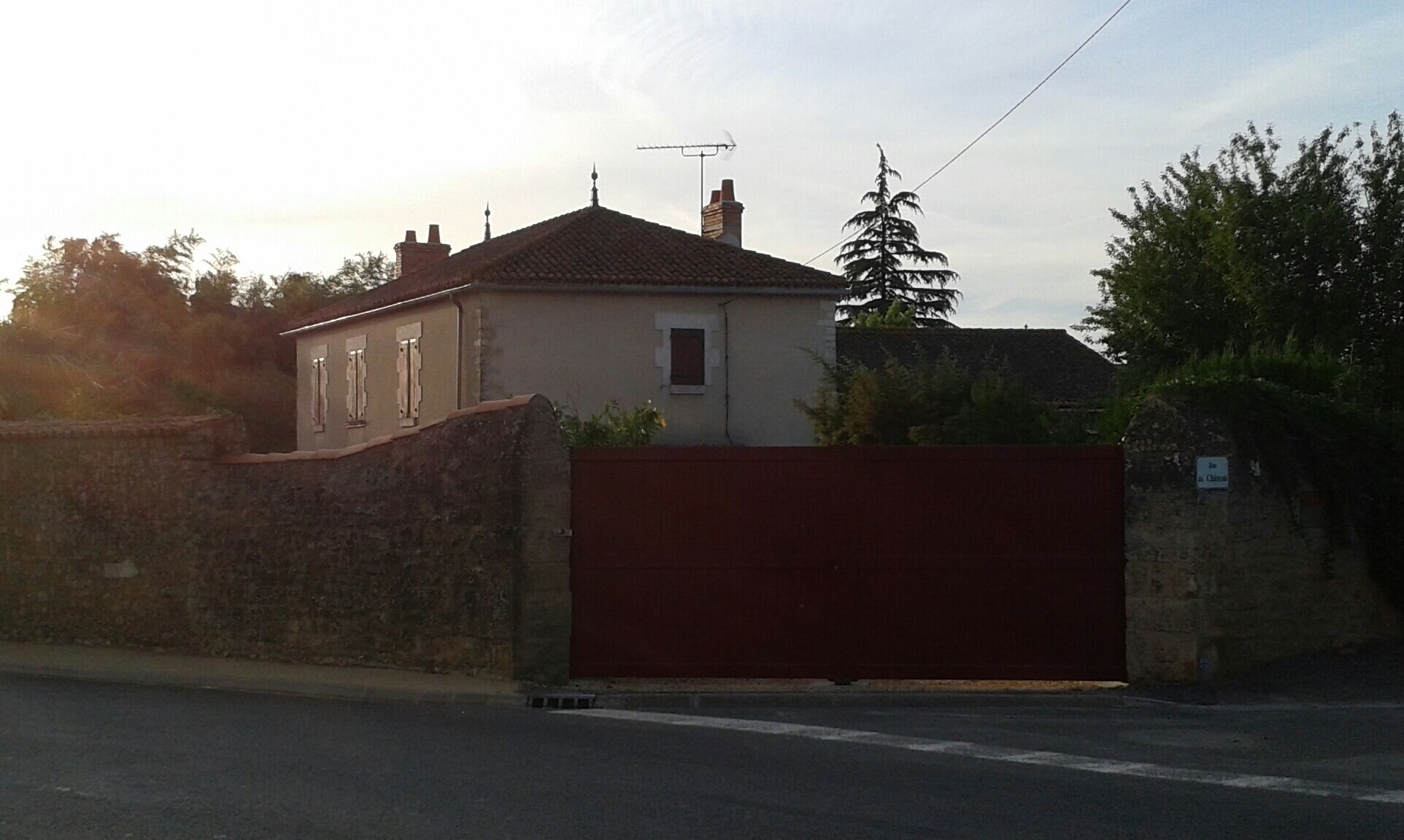 A house with a red gate, a stone wall, and a chimney.