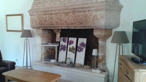 A living room with a stone fireplace, a wooden table, a sofa, and a television on a wooden cabinet. - COUNTRY HOUSE WITH LARGE GARDEN + PRIVATE POOL + RIVER (La Grimaudière)
