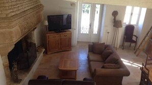 A living room with a fireplace, a sofa, a television, and a door leading outside. - COUNTRY HOUSE WITH LARGE GARDEN + PRIVATE POOL + RIVER (La Grimaudière)