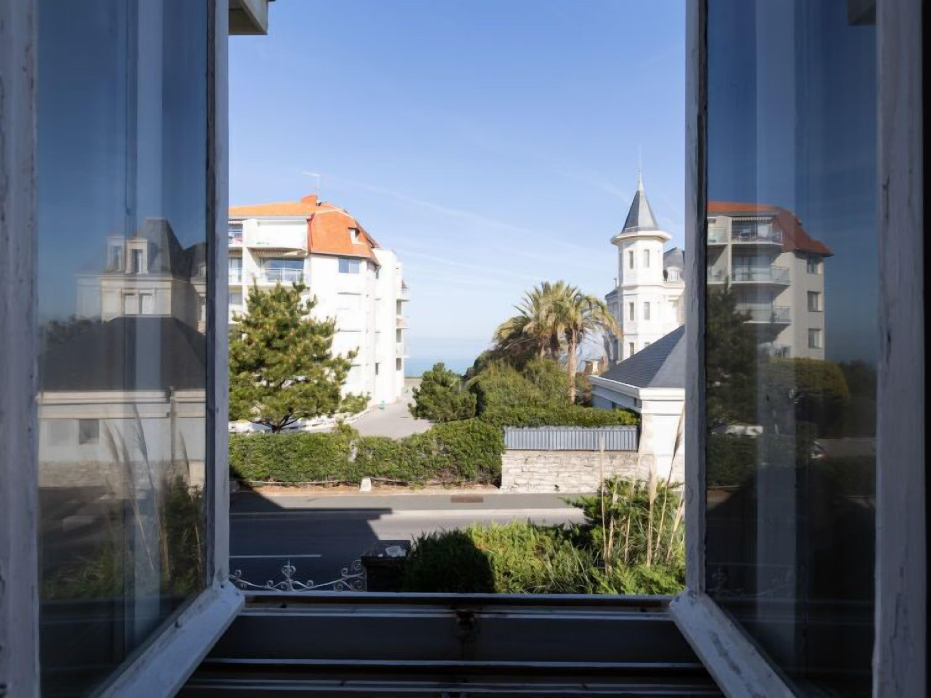 A view from a window overlooking a street with buildings, including a white building with a red roof and a tower.
