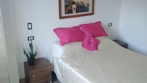 Ein ordentlich eingerichtetes Schlafzimmer mit einem Bett, einem Nachttisch mit einem Blumentopf und einem gerahmten Bild an der Wand.