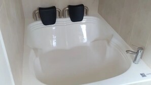 Eine große, weiße Badewanne mit einem Wasserhahn und einem Drehregler.