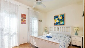 A bedroom with a bed, curtains, a ceiling fan, a painting, a nightstand, and a tiled floor. - Belle Vue by Interhome (Almuñécar)