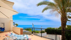 A balcony with two lounge chairs, a small table, and a hanging chair. A palm tree is visible in the background, and the balcony overlooks a scenic view of the sea. - Belle Vue by Interhome (Almuñécar)