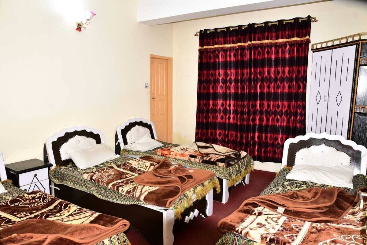 Ein Zimmer mit zwei Betten, jeweils mit gemusterten Bettbezügen und Kopfteilen. Eine Tür und ein Vorhang mit geometrischem Muster sind ebenfalls vorhanden.