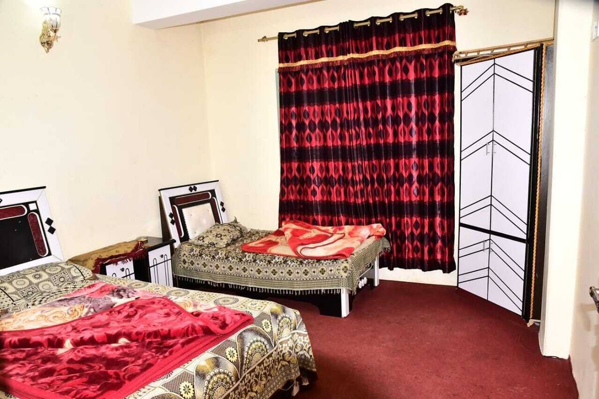 Ein Schlafzimmer mit zwei Betten, einem roten Teppich, einer gemusterten Bettdecke und einem schwarz-roten Vorhang.