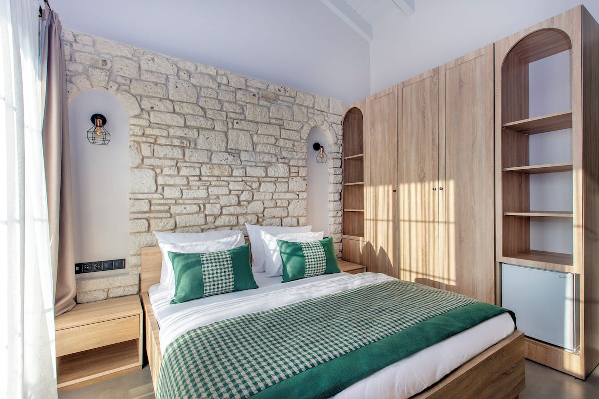 Un dormitorio con pared de piedra, armario de madera y cama con ropa de cama verde.