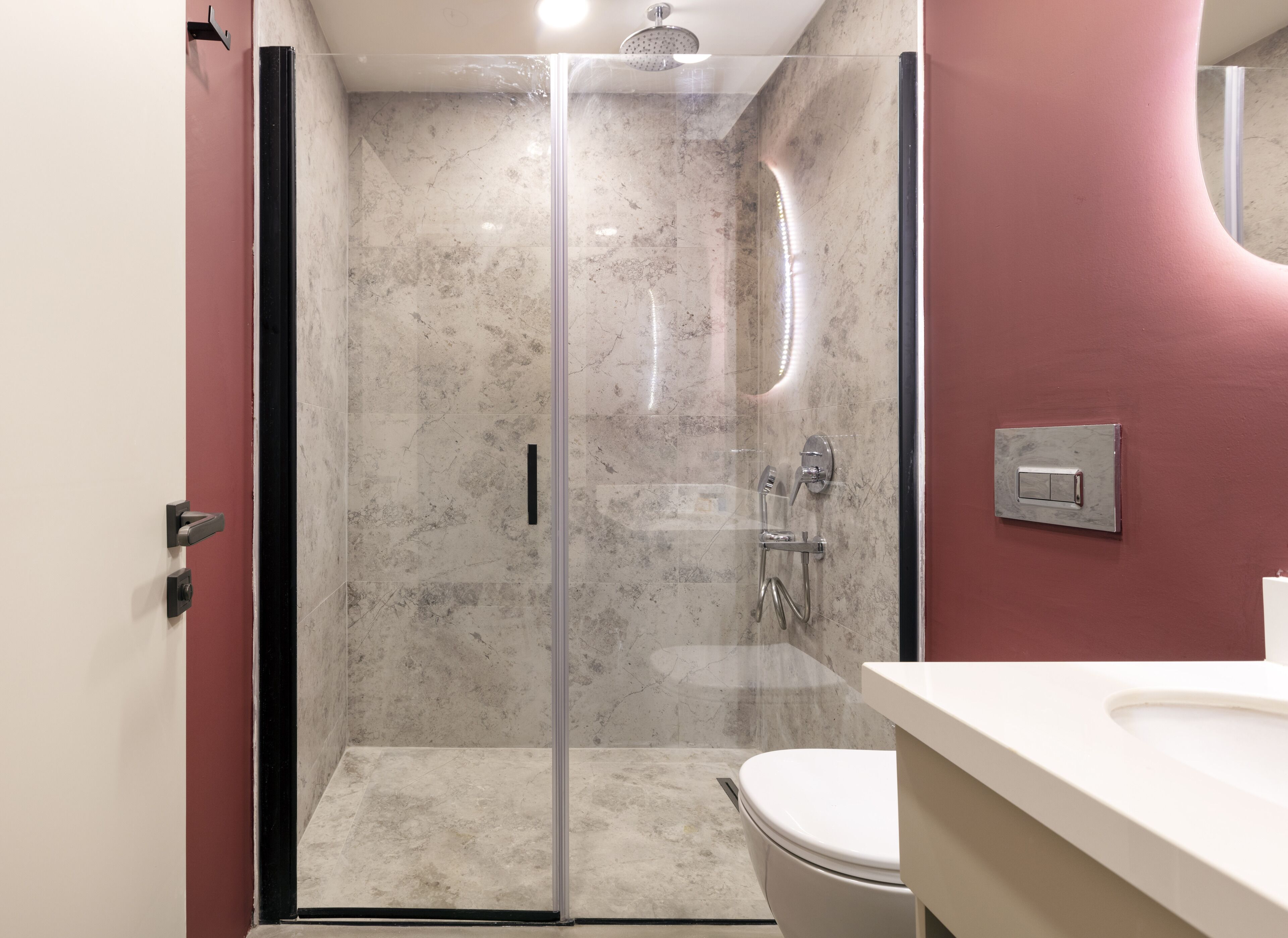 A modern bathroom with a glass-enclosed shower, a white toilet, and a marble-tiled wall.