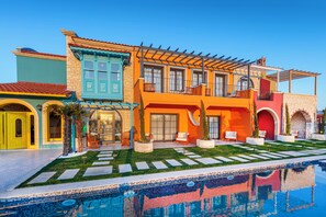 Un edificio colorido con piscina, mobiliario exterior y un jardín bien cuidado.
