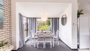 Un comedor con una mesa preparada para cuatro, una lámpara colgante y vistas al exterior con vegetación.