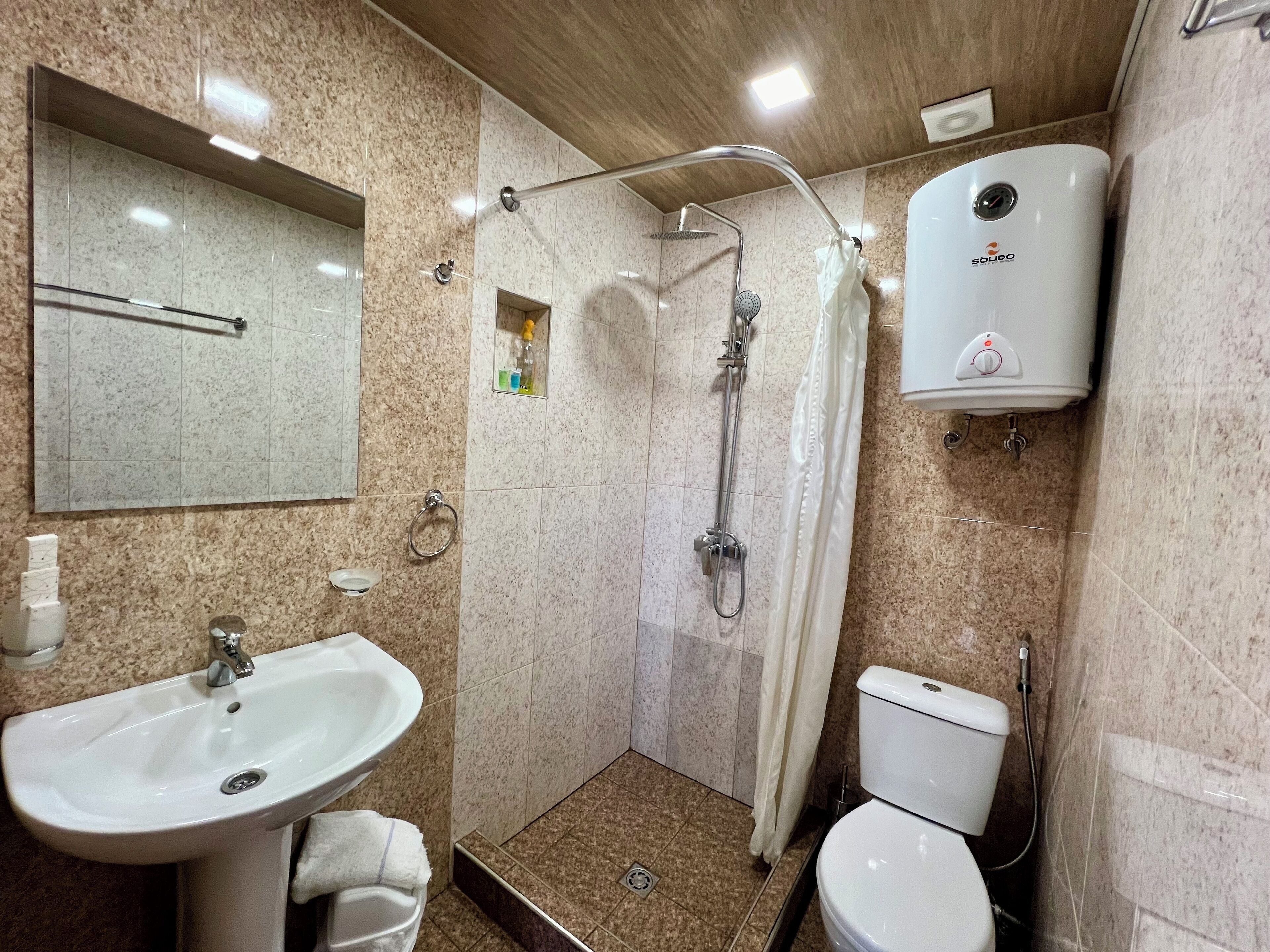 A bathroom with a sink, toilet, shower, and a hand dryer.