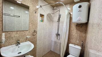 A bathroom with a sink, toilet, shower, and a hand dryer.