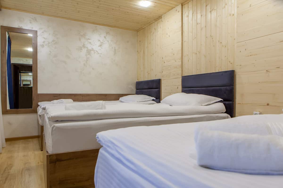 A hotel room with wooden panel walls, two beds with white linens, a large mirror, and a wooden floor.