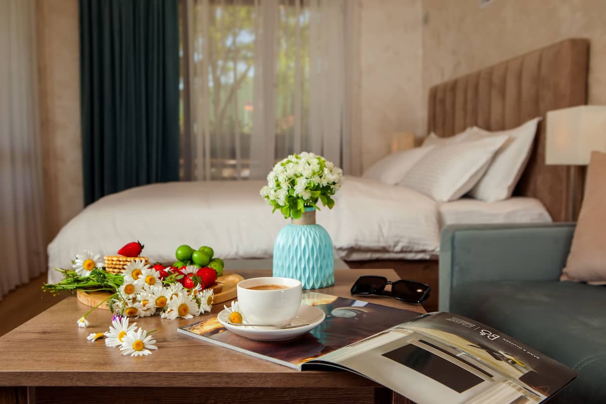 A neatly arranged hotel room with a bed, a coffee table with flowers, fruits, and a magazine.