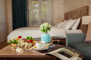 Habitación de hotel ordenada con una cama, una mesita de café con flores, frutas y una revista.
