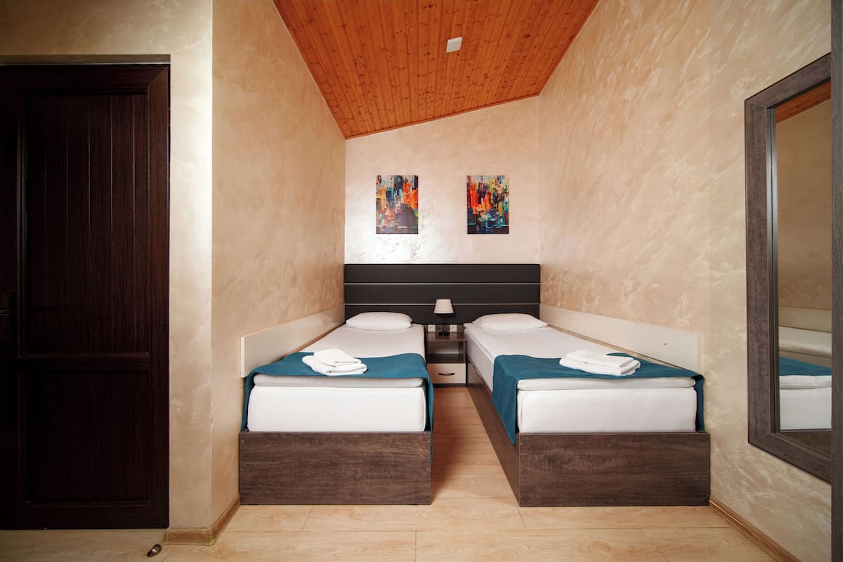 A room with two beds, wooden headboards, a nightstand, a mirror, and two paintings on the wall.