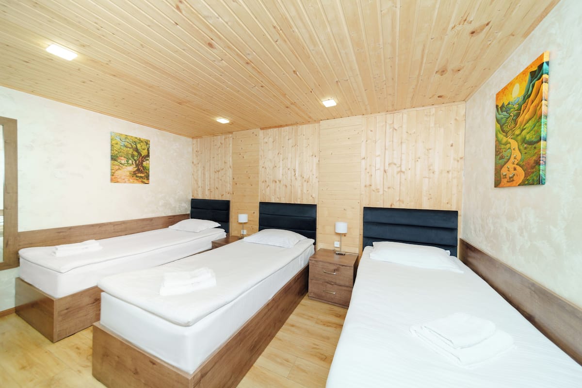 A room with three single beds, wooden walls, and ceiling, and two paintings on the walls.
