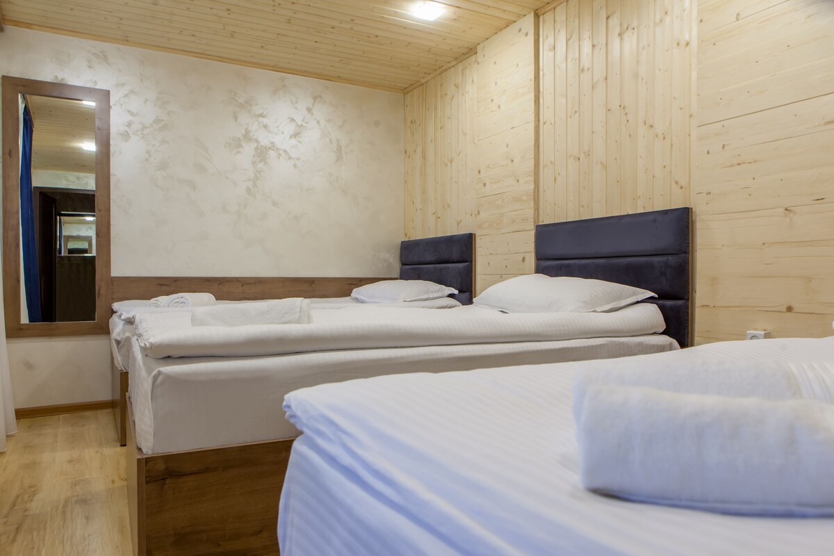 A hotel room with wooden panel walls, two beds with white linens, a large mirror, and a wooden floor.