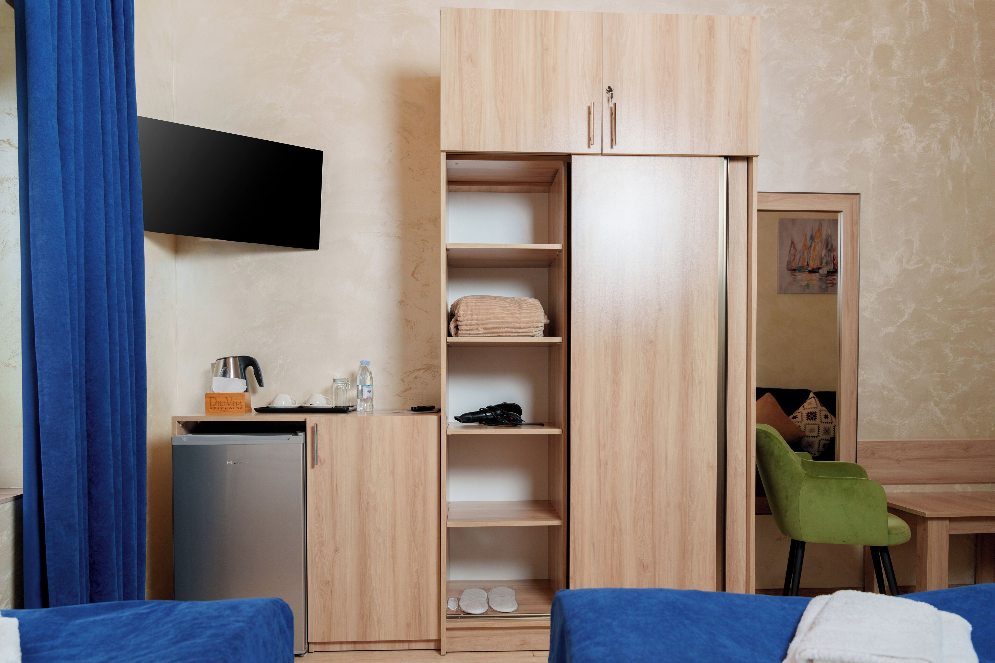 A hotel room with a bed, a desk, a wardrobe, a small fridge, and a chair.
