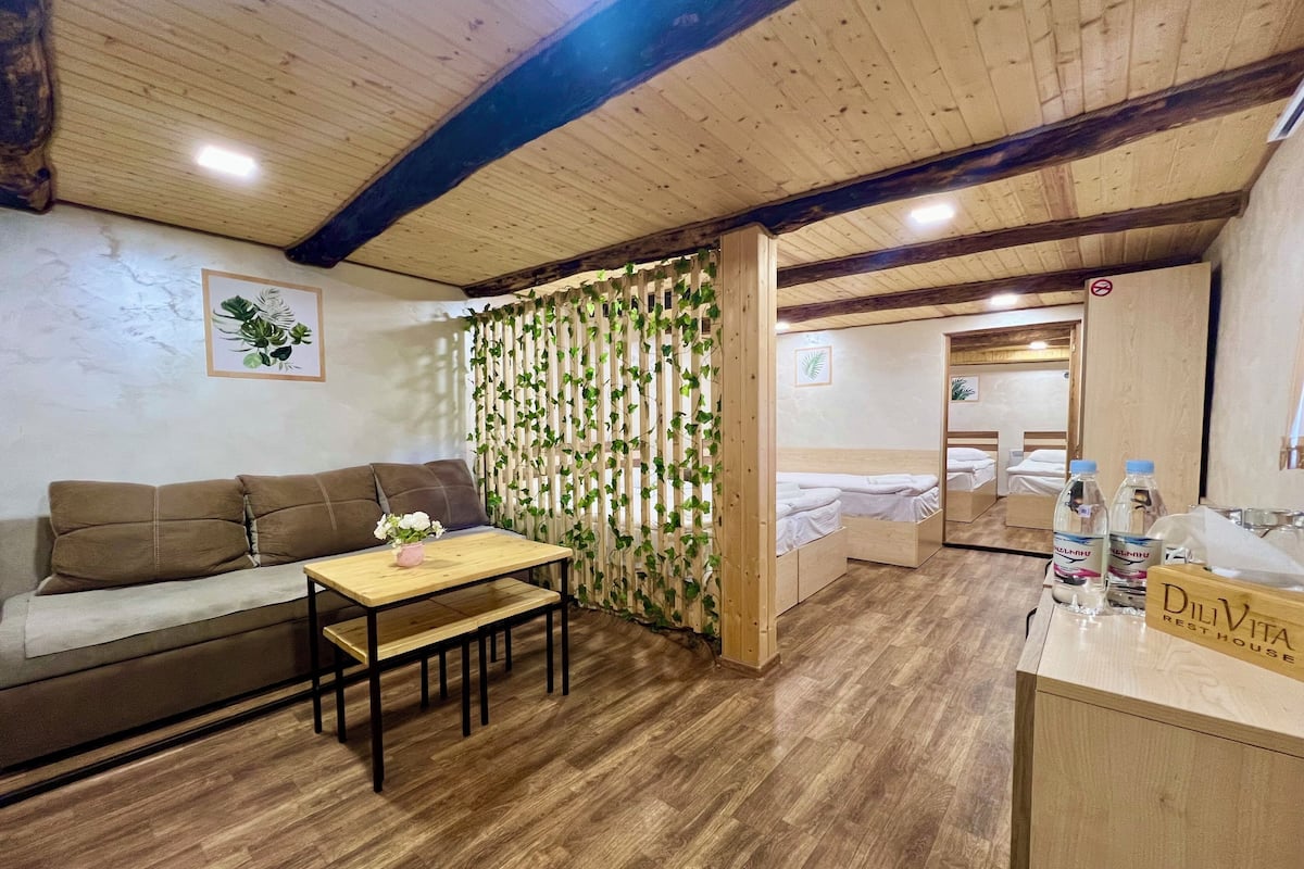 A cozy room with a wooden ceiling, a sofa, a small table with a vase, and a bed with a wooden headboard.