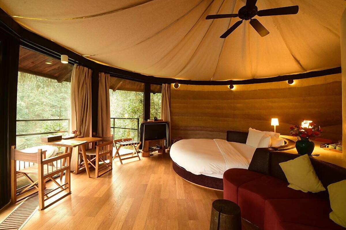 Une pièce confortable avec un lit, un canapé rouge, une table à manger avec des chaises, un ventilateur de plafond et un téléviseur.