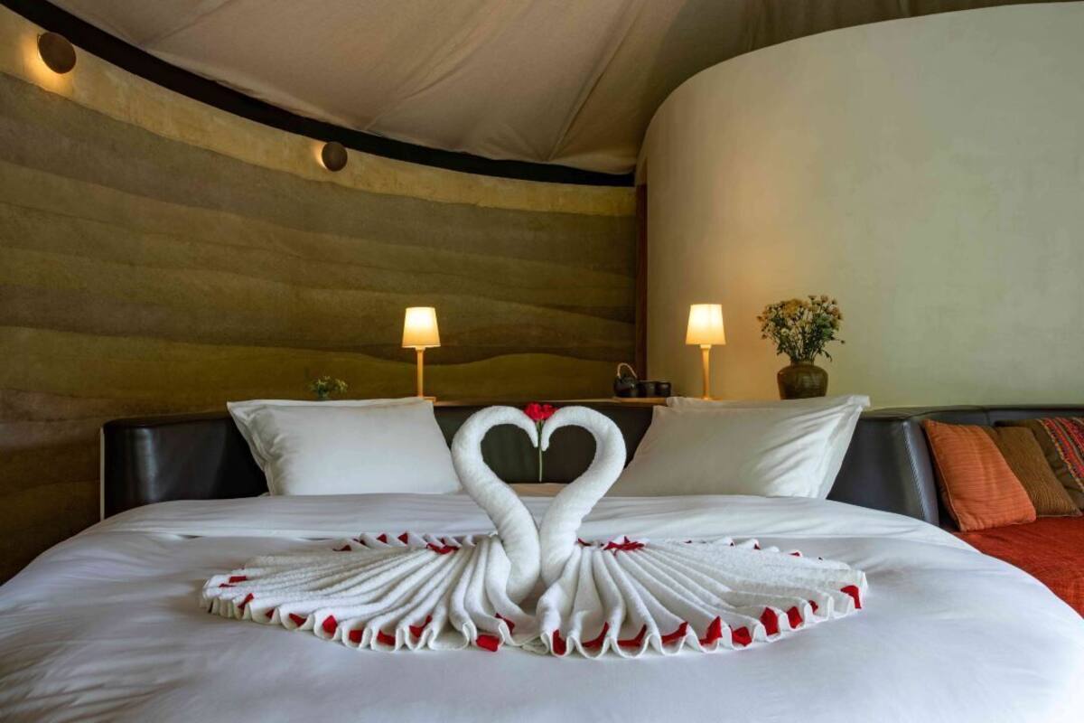 Une chambre d’hôtel avec un lit agrémenté d’une décoration en forme de cœur réalisée avec des serviettes, ainsi que deux lampes de chevet.