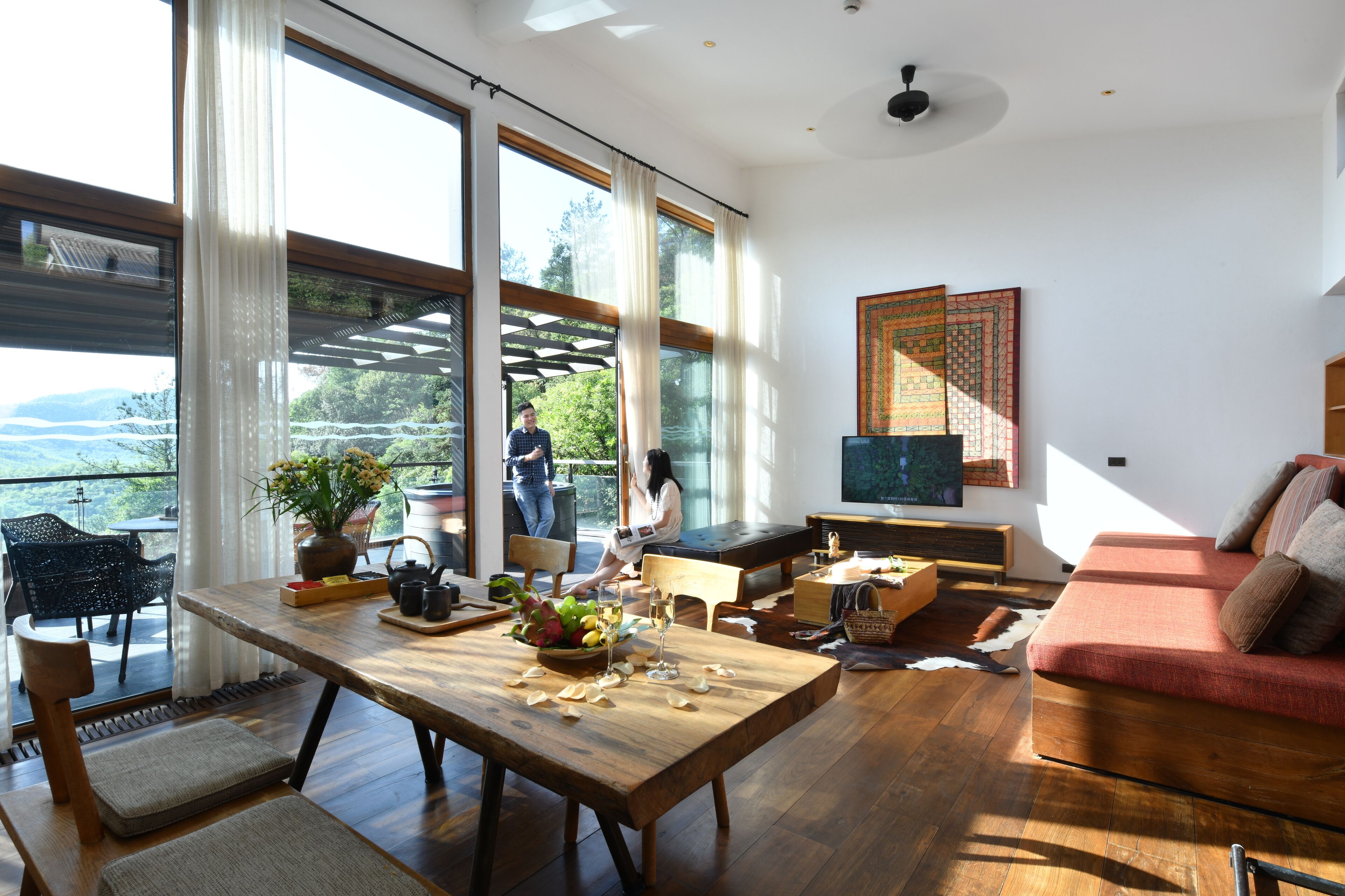A spacious living room with a large wooden table, a sofa, and a TV mounted on the wall.