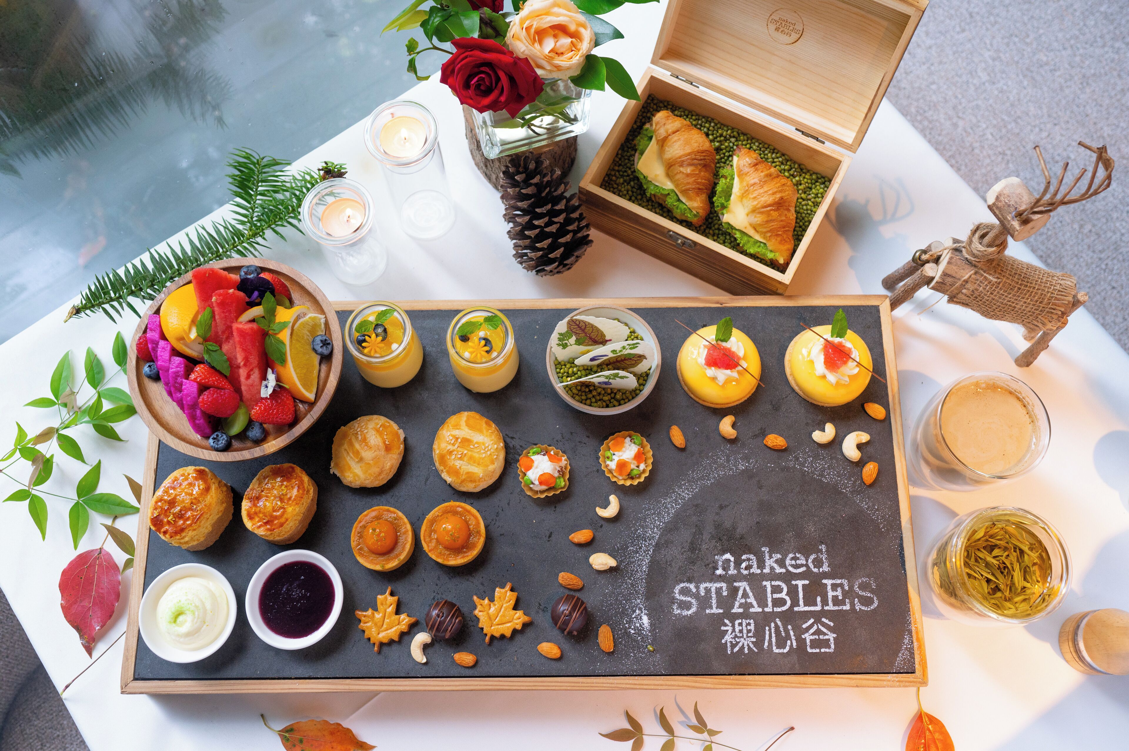 Una mesa de postres con diferentes pasteles y frutas, una vela y un reno decorativo.
