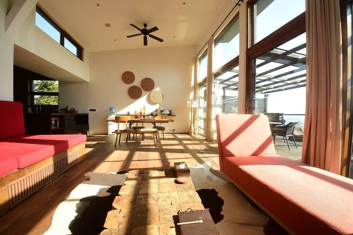 Un vaste espace de vie comprenant un canapé rouge, une table à manger en bois et un ventilateur de plafond.