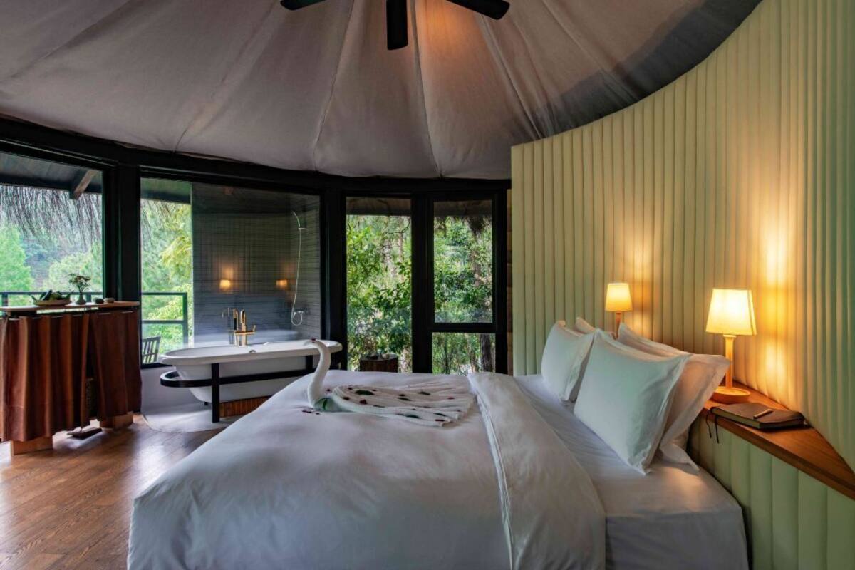 Une chambre à coucher avec un grand lit, une coiffeuse avec un miroir, une baignoire et une fenêtre donnant sur un paysage verdoyant.