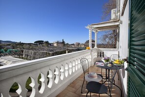 Een balkon met een witte reling, een tafel met stoelen en een uitzicht op de stad.
