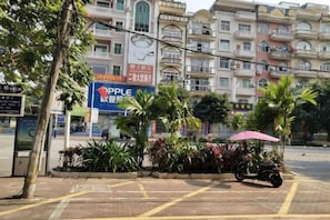 A multi-story building with commercial signage, a parking area with a scooter, and a small garden with palm trees.