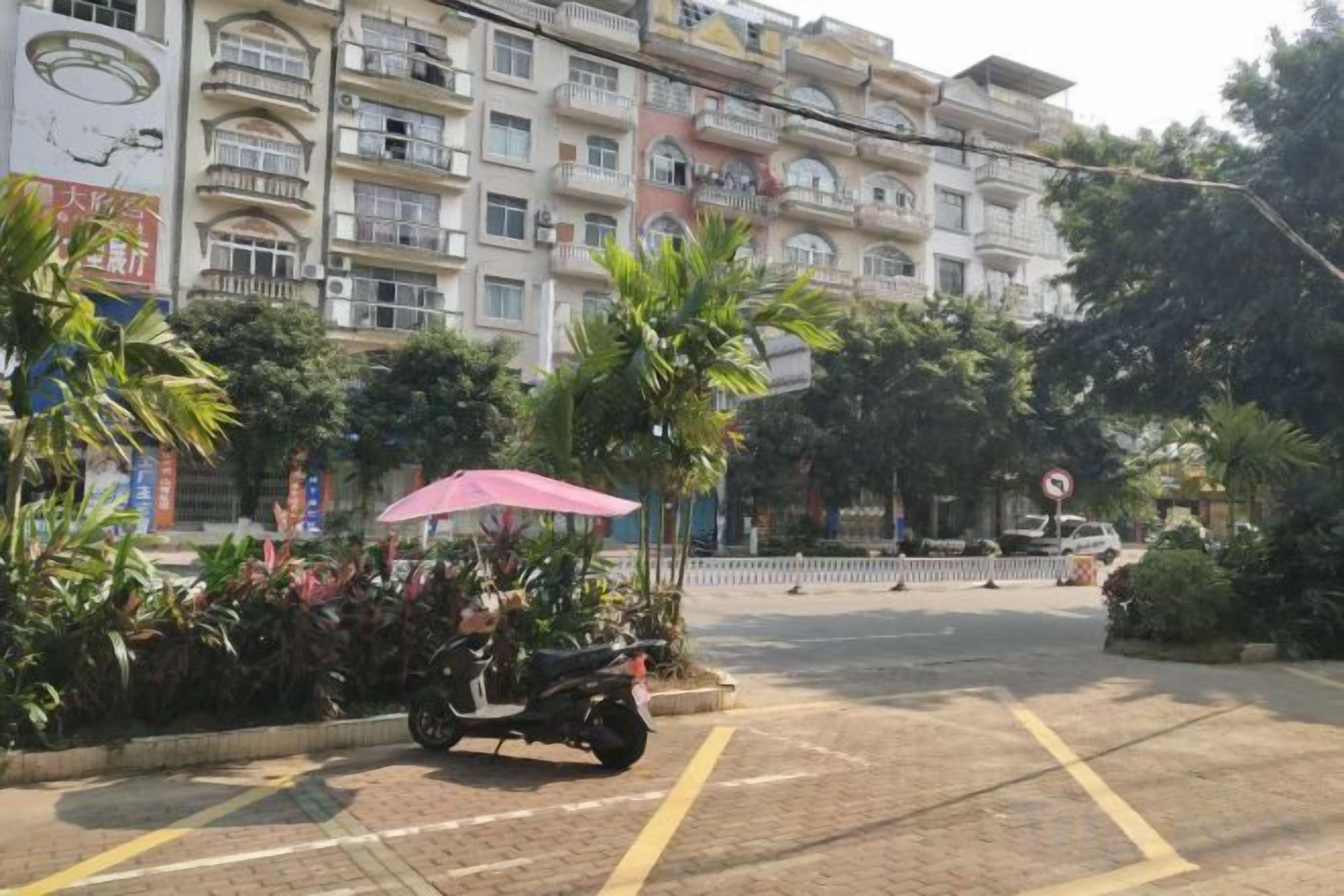 Un immeuble à plusieurs étages doté de balcons, un scooter garé et un passage piéton.