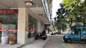 A street view with a building that has a sign in a foreign language, a parked scooter, and a delivery truck. - Youxian Bianjie Hotel (Dongxing)