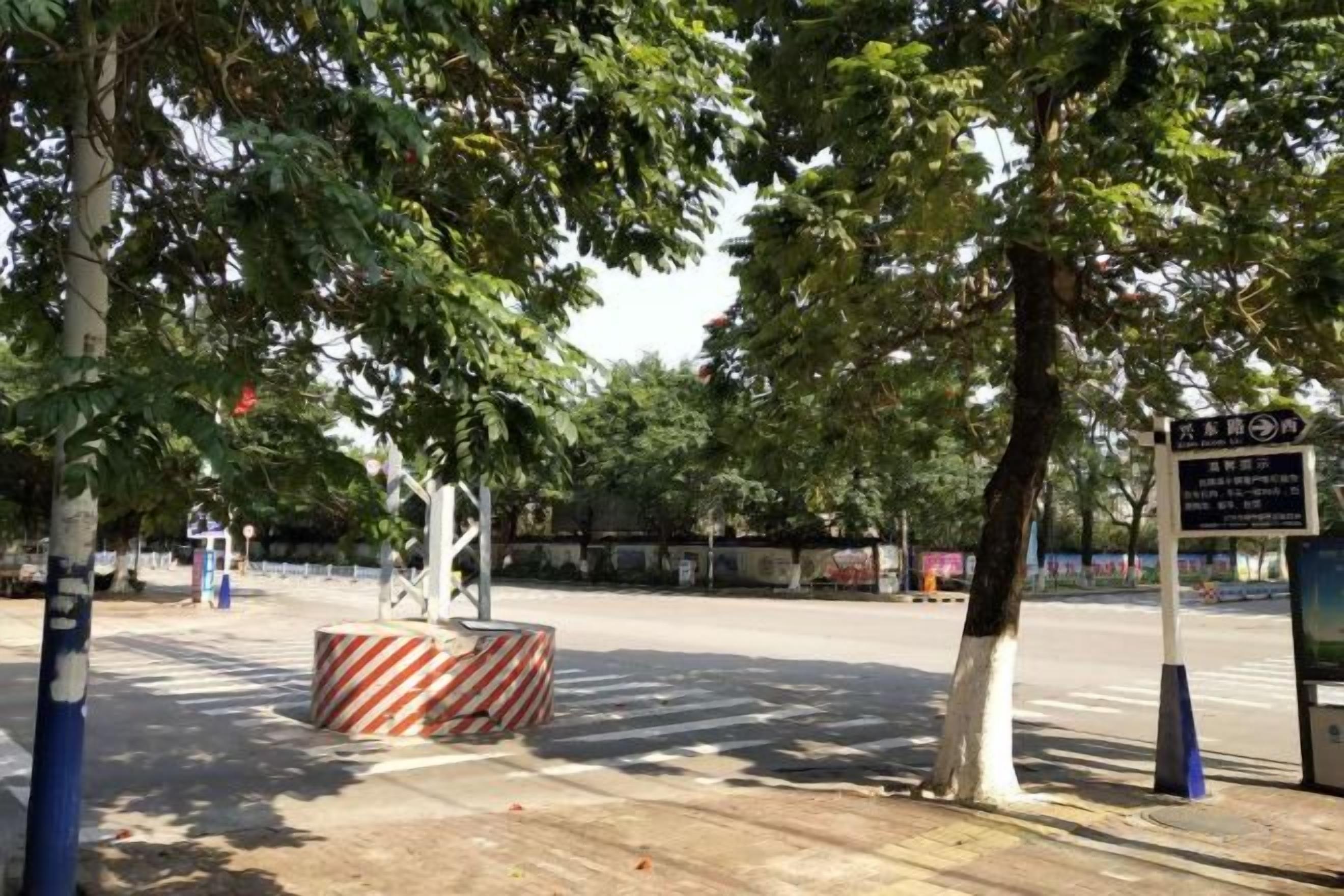 A tree-lined street with a striped barrier and directional sign.