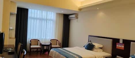 Une chambre d’hôtel avec deux lits, un bureau avec une chaise, une télévision et une fenêtre avec des rideaux.