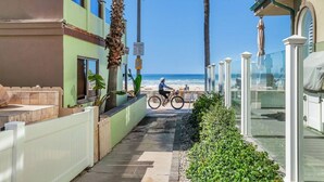 A coastal street with a cyclist, a beach in the background, and a building with a balcony.